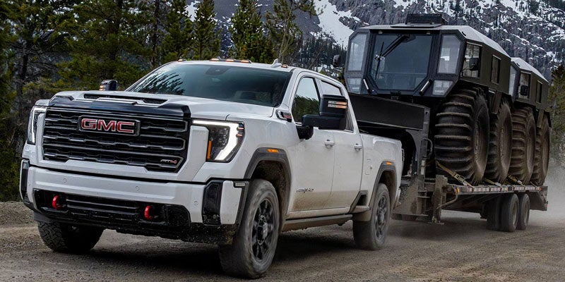 White GMC heavy-duty pickup truck towing a large tracked off-road
