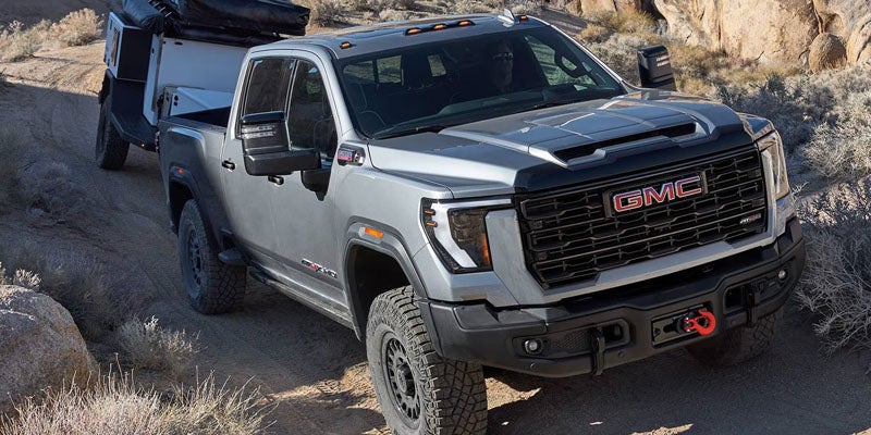 Gray GMC heavy-duty pickup truck driving on a rugged dirt trail while towing a camper trailer